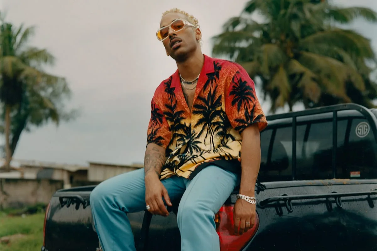 Laylow assis sur un pick-up en chemise à fleurs