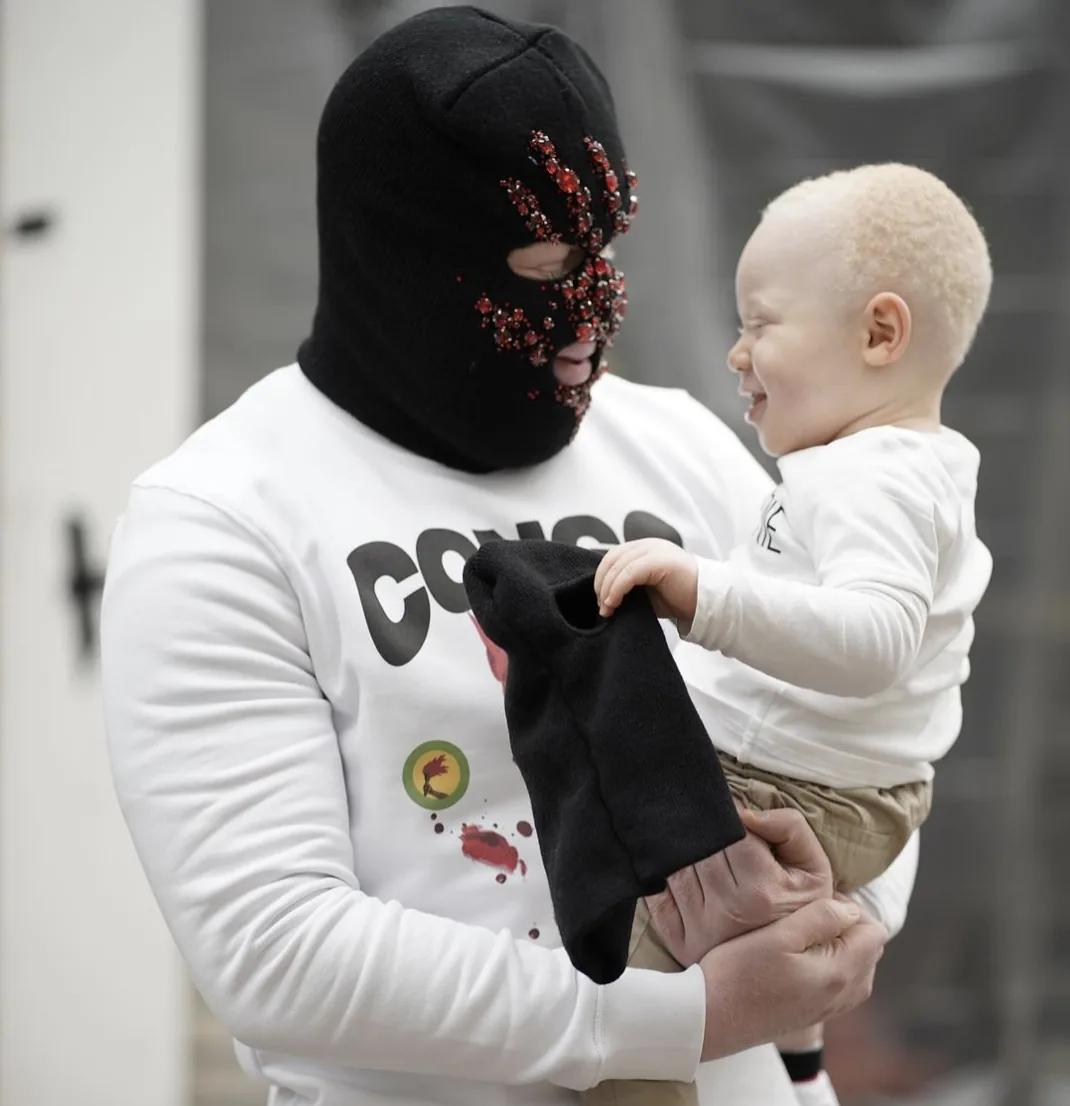 Kalash Criminel cagoulé portant un enfant